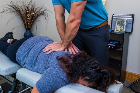 Chiropractor adjusting a patient's back on an examination table. The patient is lying face down.