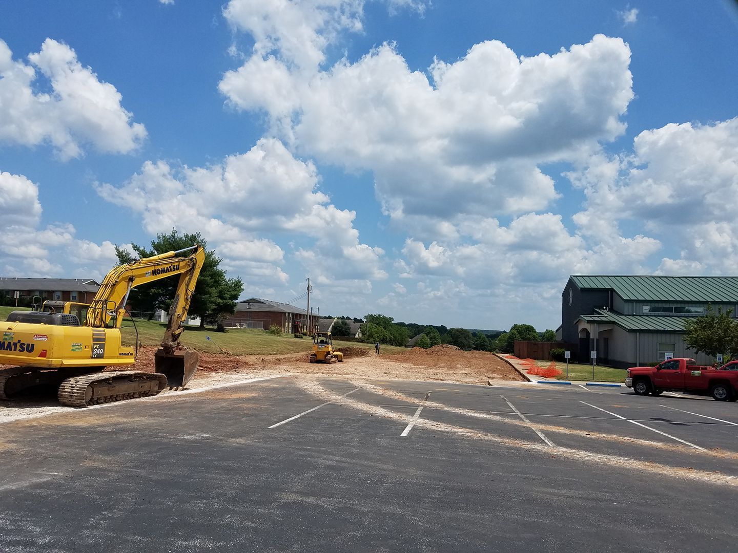 A yellow excavator is parked in a parking lot next to a red truck.