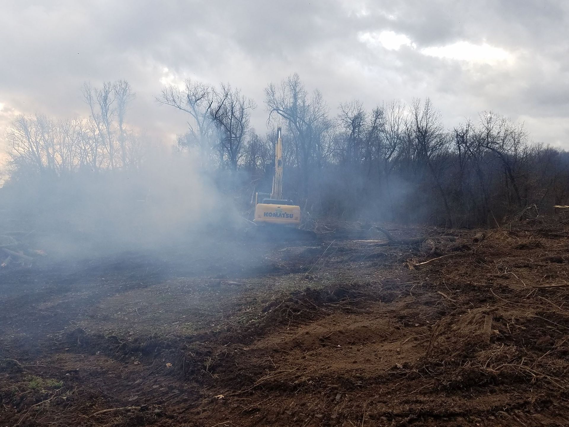 A bulldozer is driving through a field with smoke coming out of it.