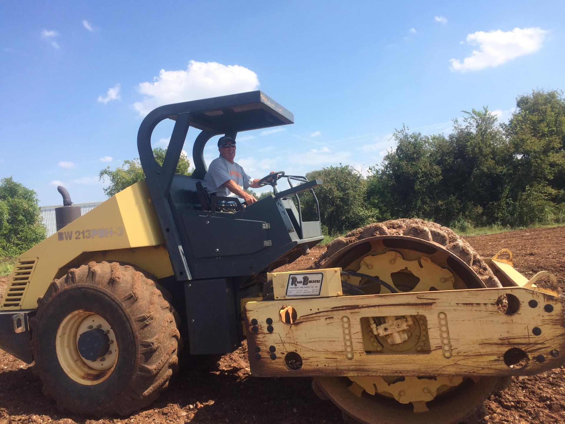 A man is driving a yellow and black tractor in a dirt field.