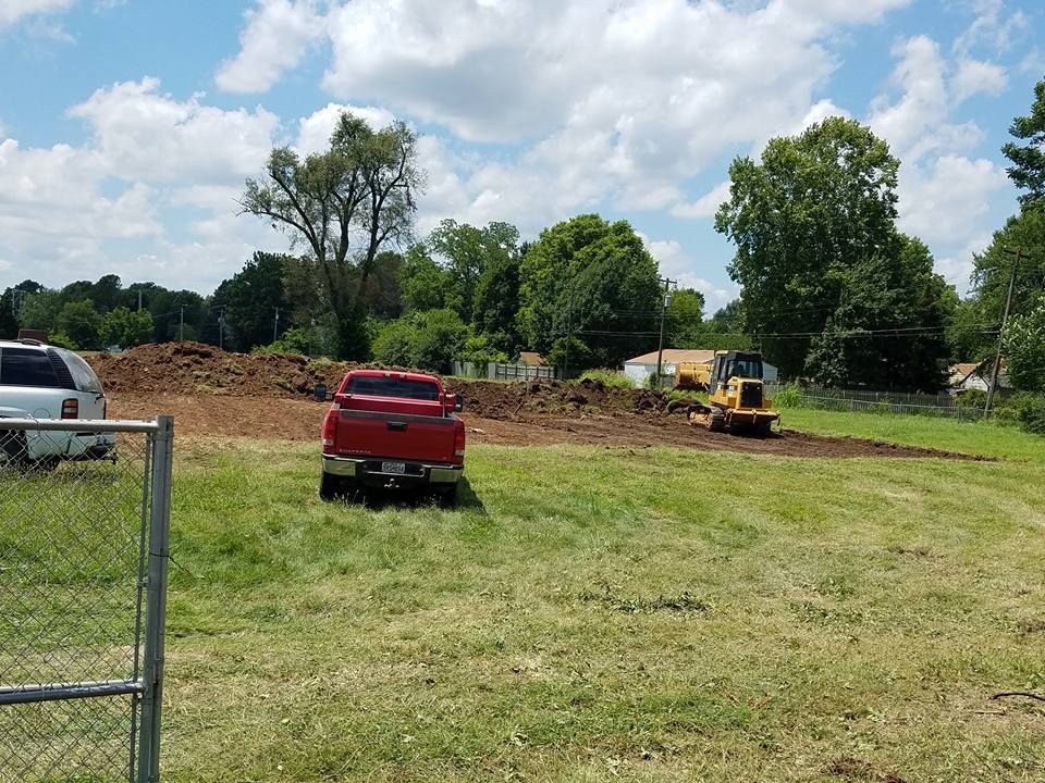 A red truck is parked in a grassy field next to a bulldozer.