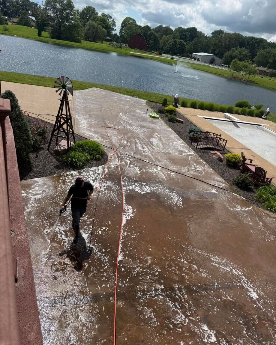 Person pressure-washing a wet patio beside a lake on a cloudy day