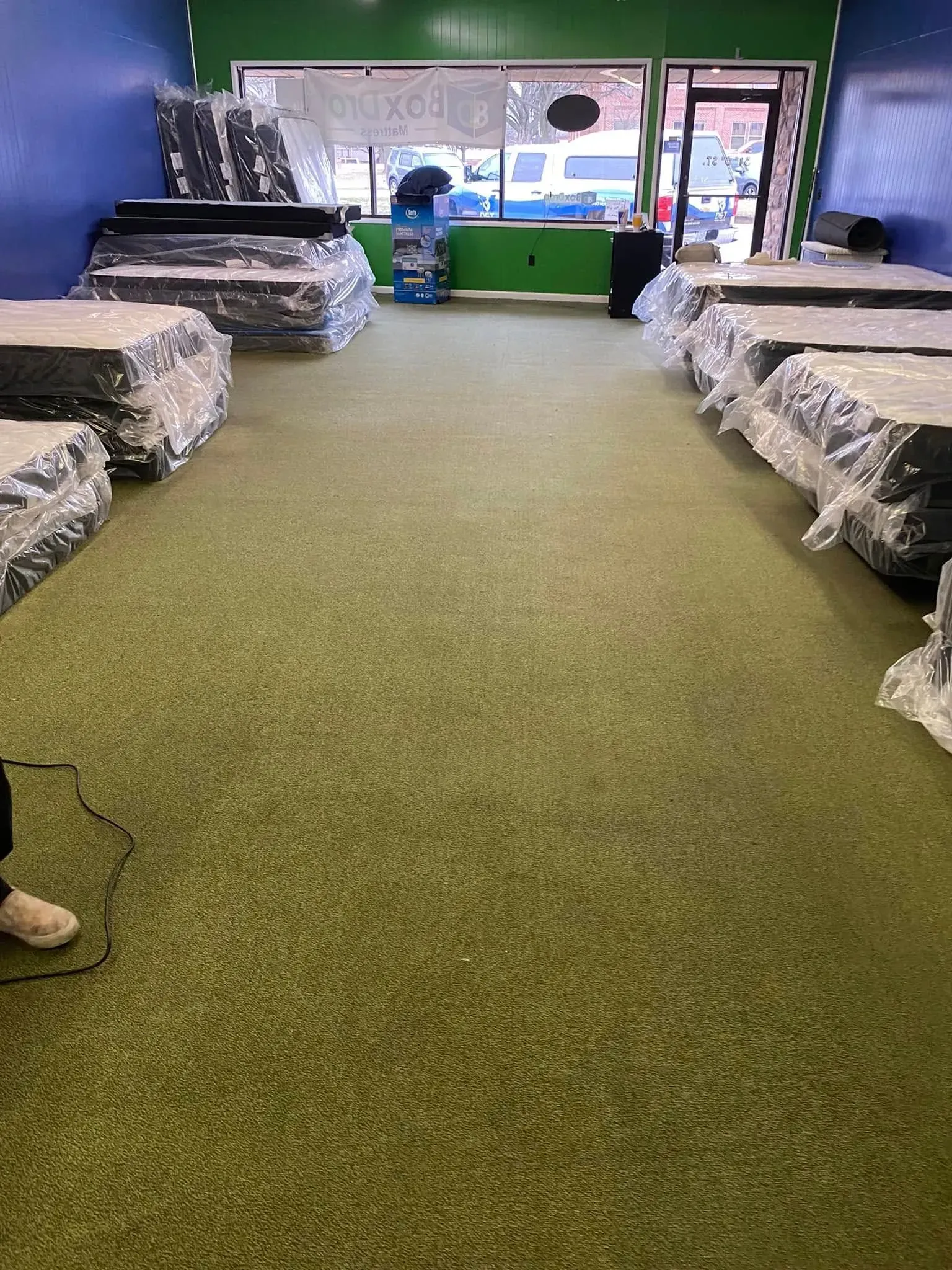 Green-carpeted room with two rows of wrapped furniture and windows at the back.