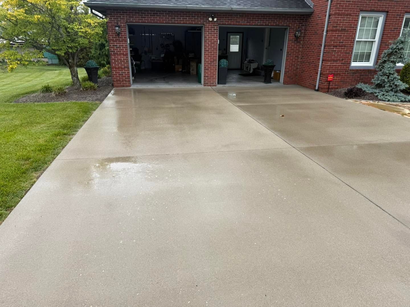 Wet concrete driveway leading to a brick house’s covered carport and front entrance