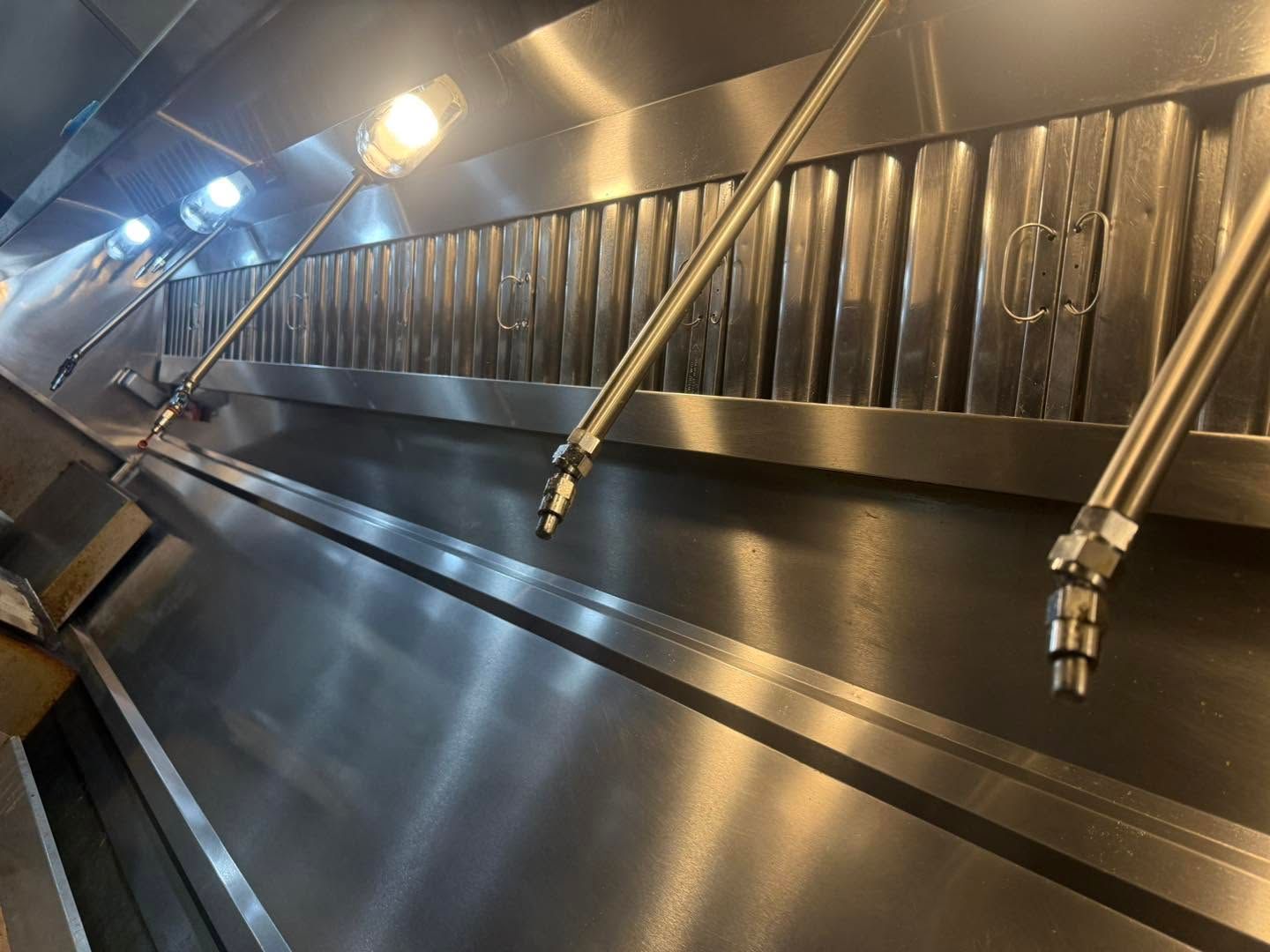 Stainless steel industrial chute with angled support bars and overhead lights