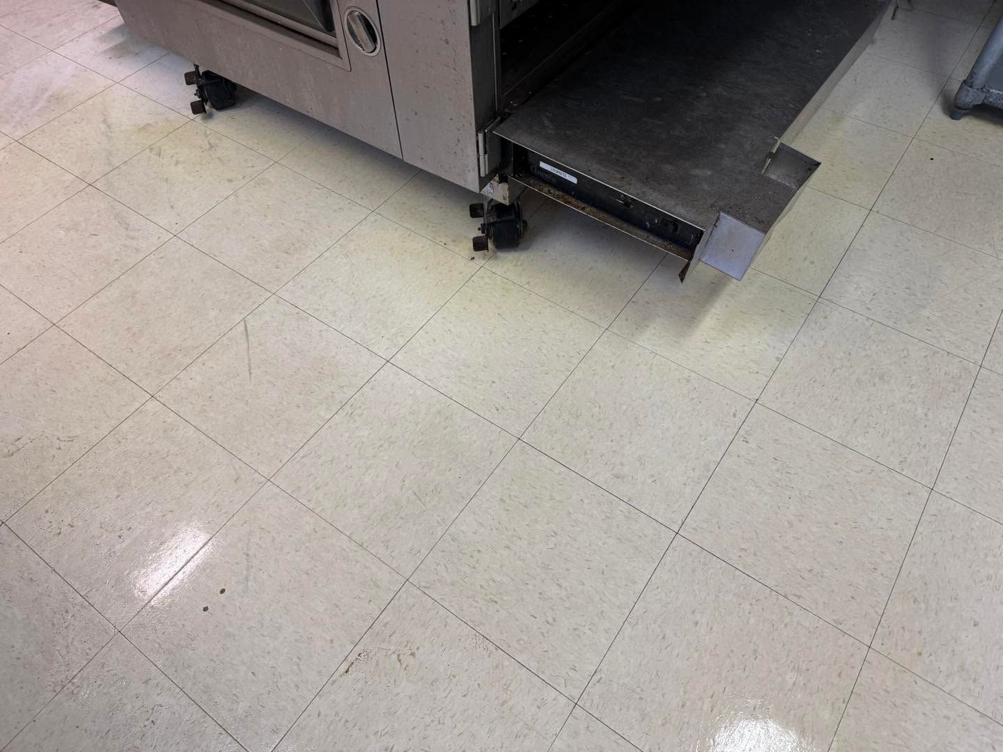 Close-up of a stainless steel machine on a tiled floor with a black wheel and metal step or ramp.
