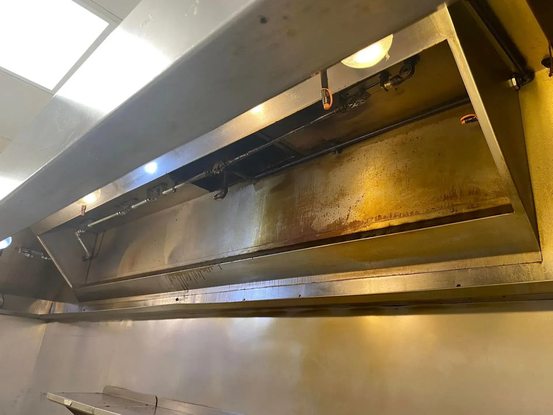 Stainless steel kitchen exhaust hood with grease filters and light reflections.