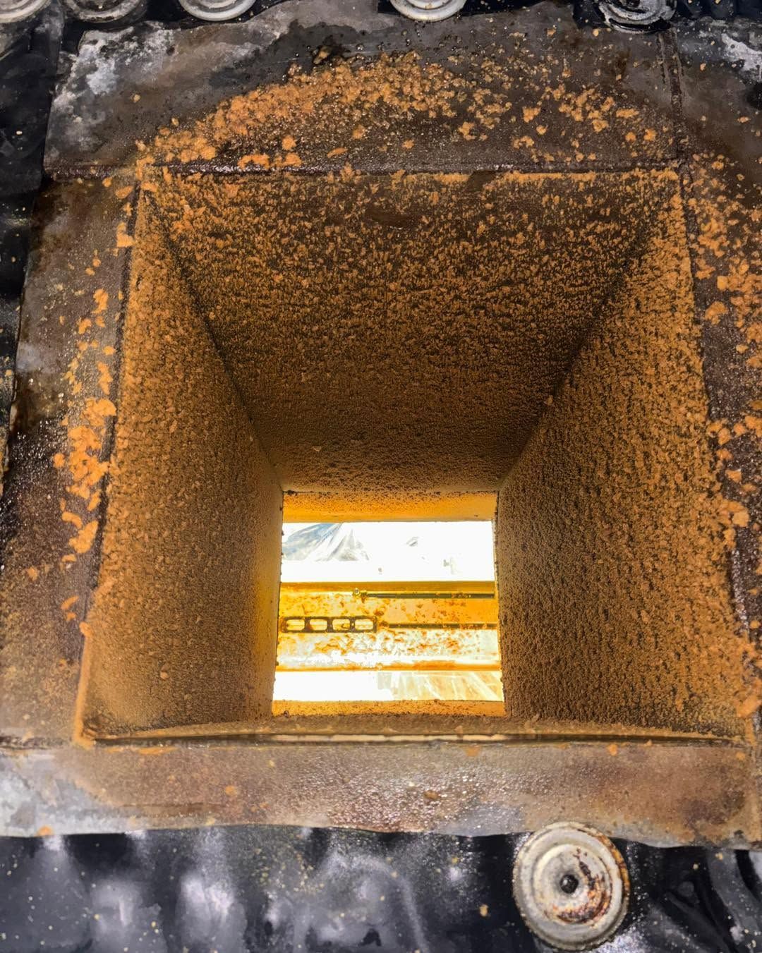 Rusty square metal chute viewed from above, with a bright opening at the bottom.