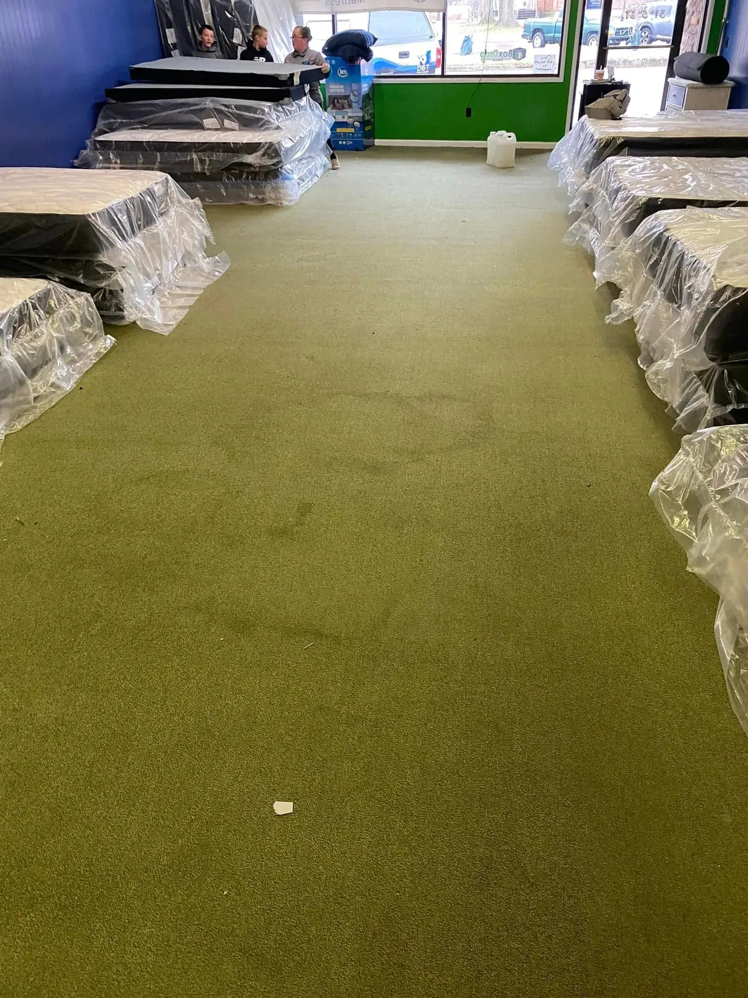 Turf-covered aisle between stacked wrapped goods in a warehouse-like room, with people near the far end.