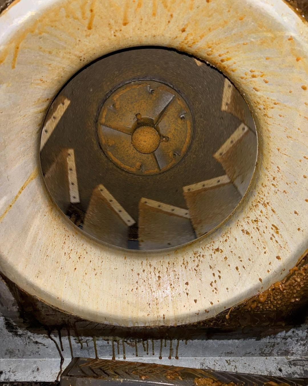 Rusty industrial hopper with circular opening and worn metal blades inside.