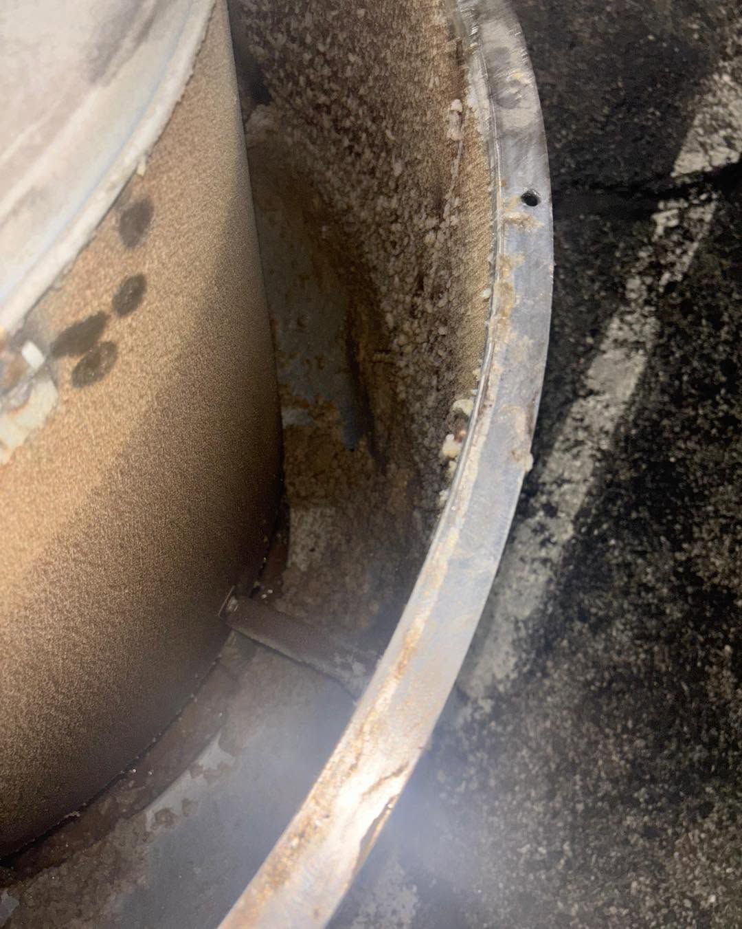 Close-up of a dirty metal pipe and circular rim with rust and grime on a concrete surface.