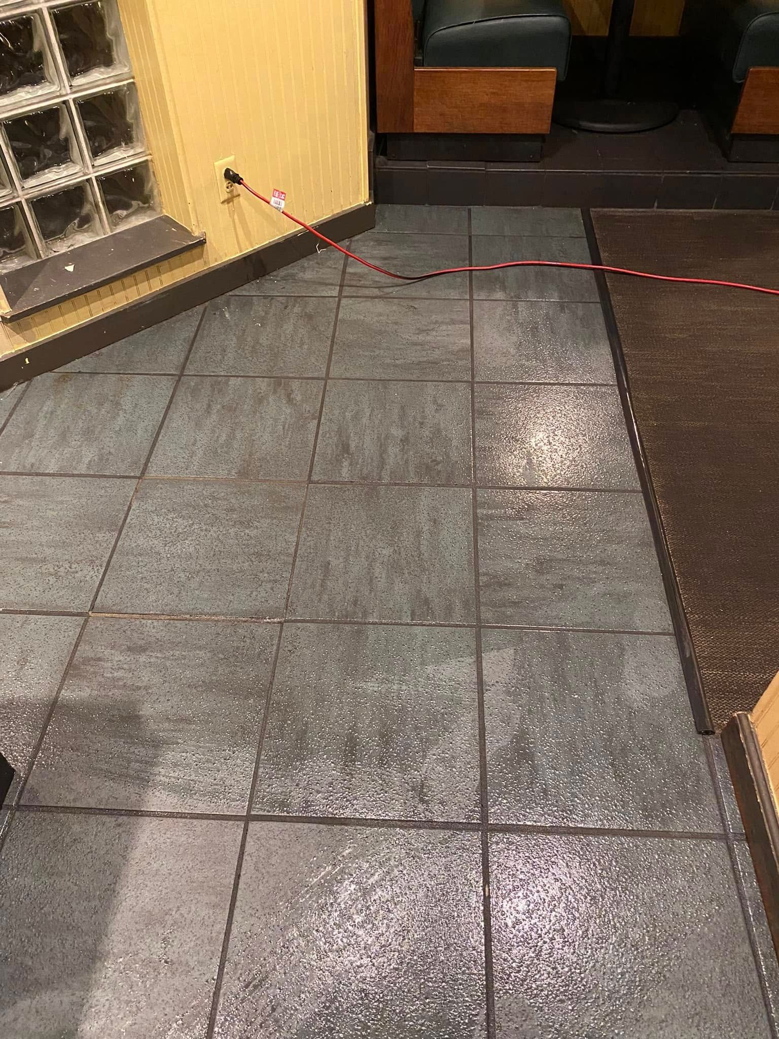 Wet tiled walkway beside a building entrance, with a red rope barrier and glass block wall.