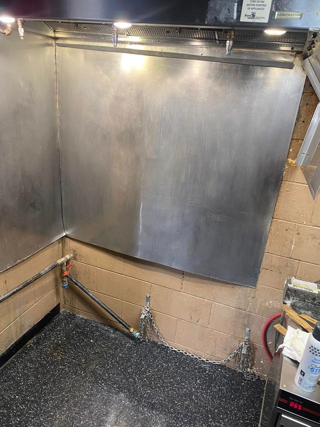 Metal wall paneling inside a room with exposed cardboard backing and a speckled black floor.