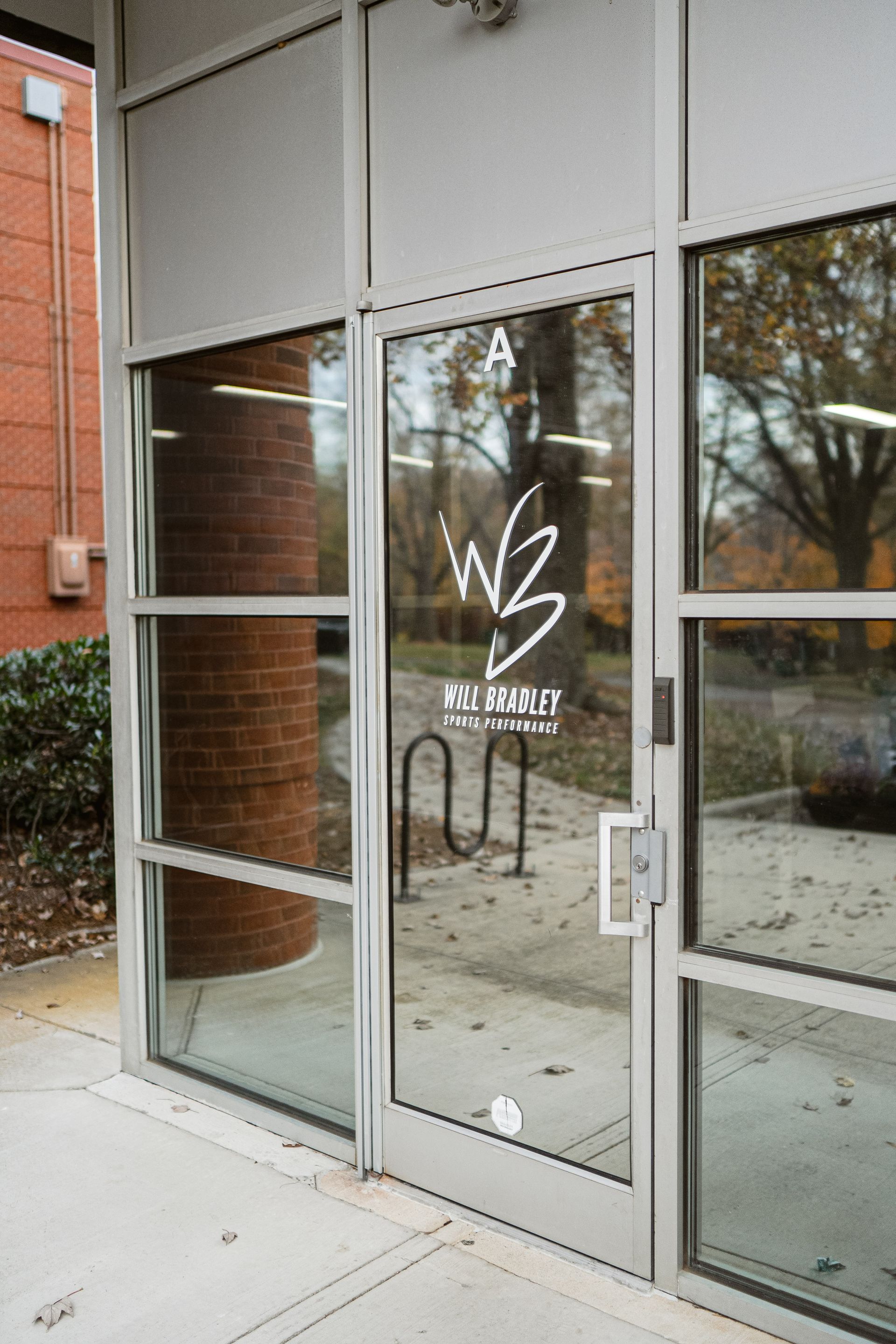 Glass storefront entrance with white logo and brick walls reflected in the doors