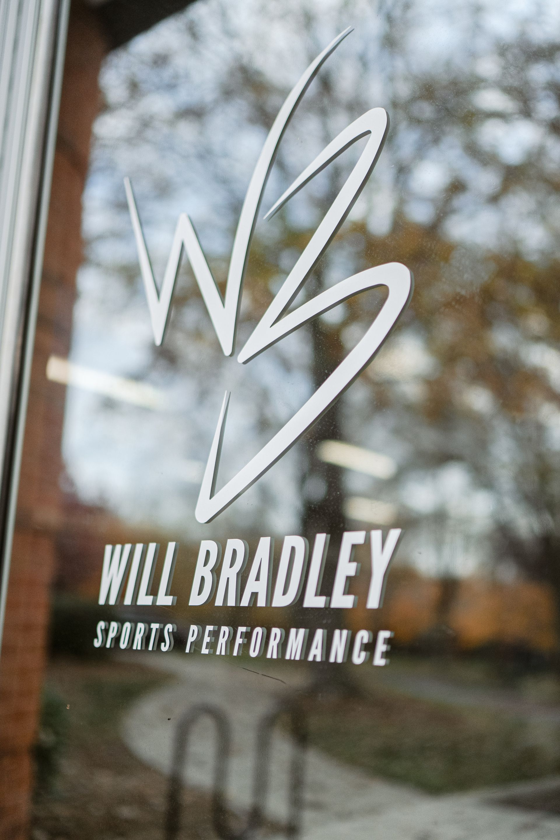 Will Bradley Sprint Performance logo on a reflective glass door with blurred trees in the background