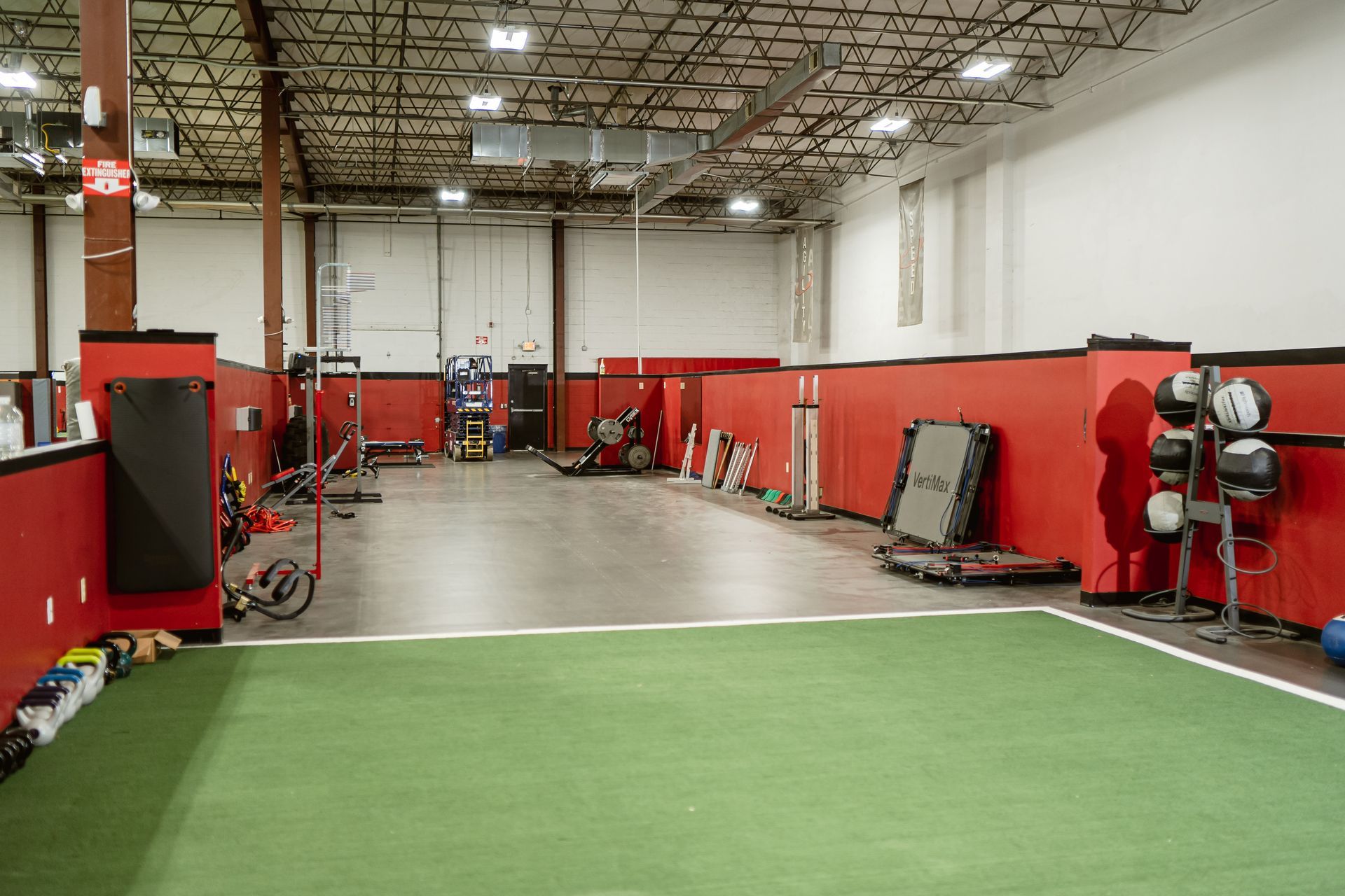 Indoor gym training area with red walls, turf floor, and equipment lining the sides