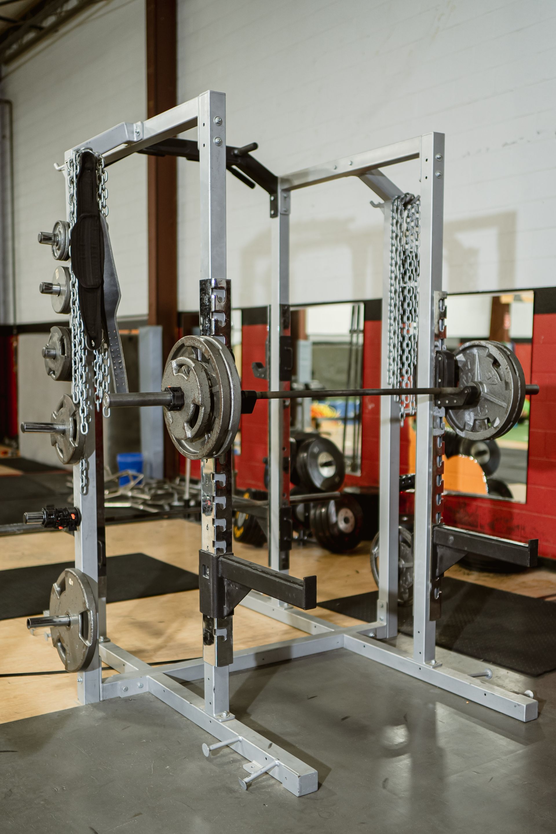Metal gym squat rack with weight plates and chains in a weightlifting room