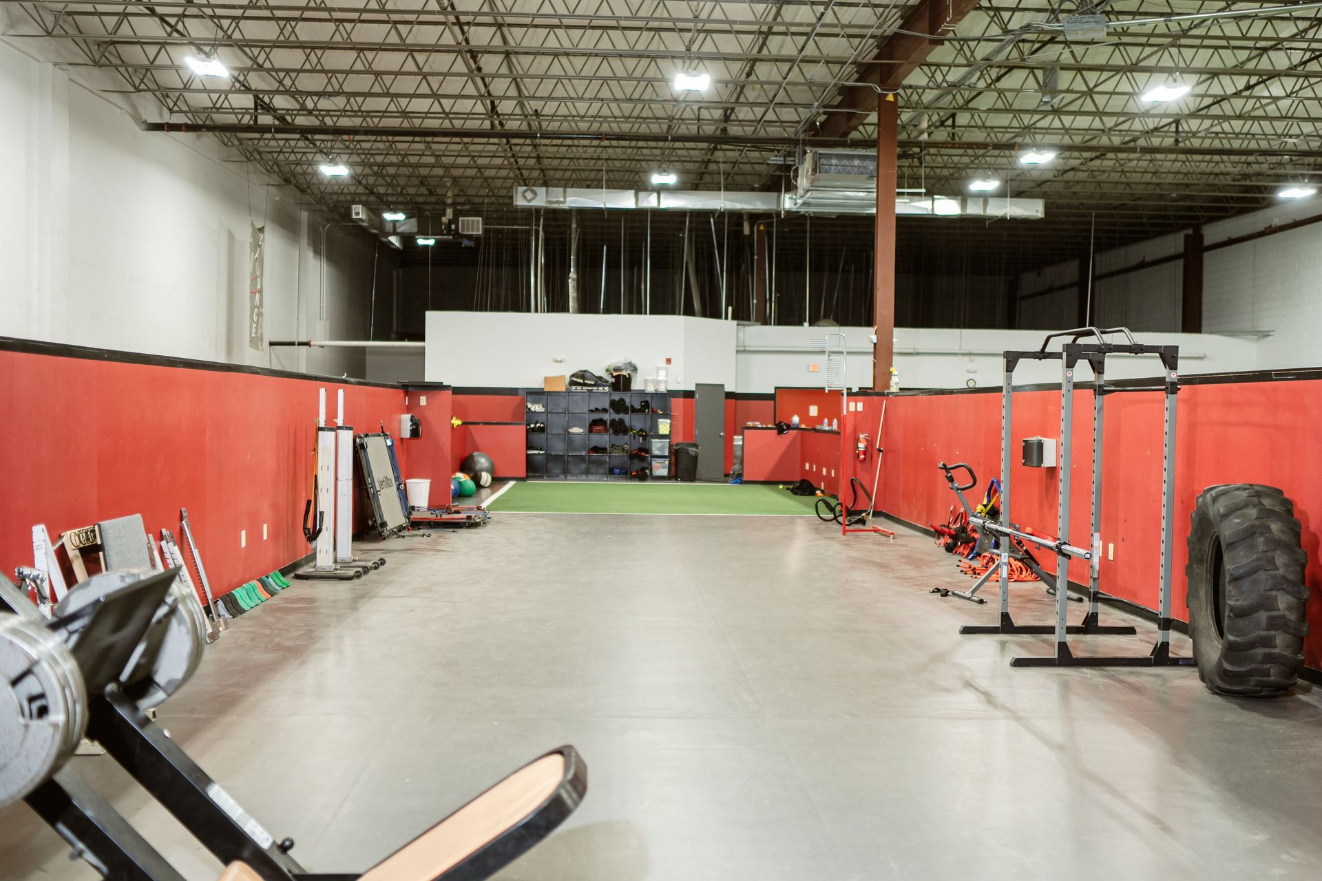 Empty gym with red walls, exercise equipment, and a large tire on the right.
