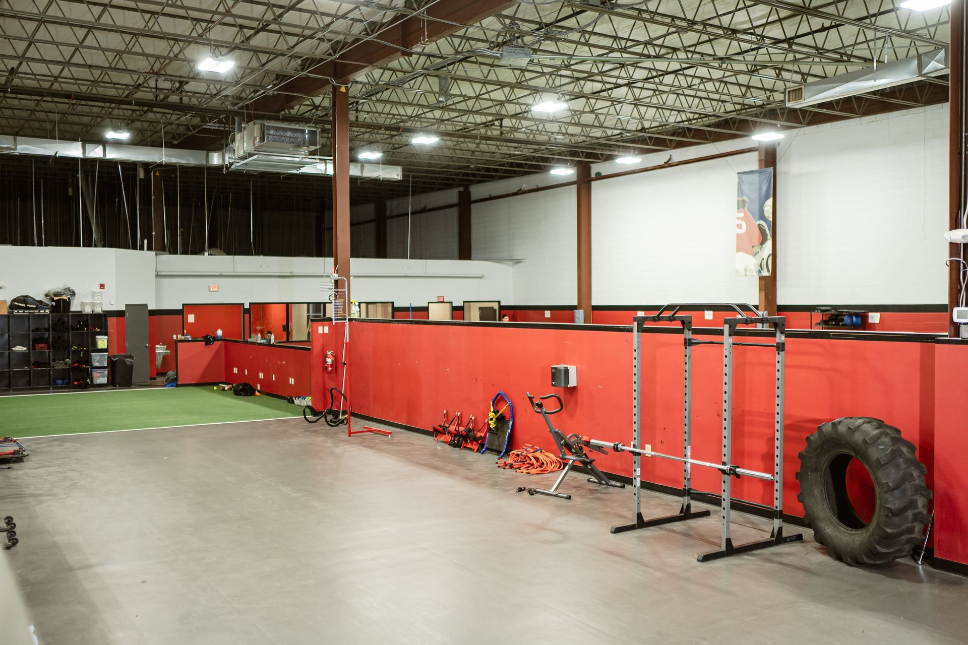 Indoor training gym with red padded walls, exercise equipment, and a large tire on the right