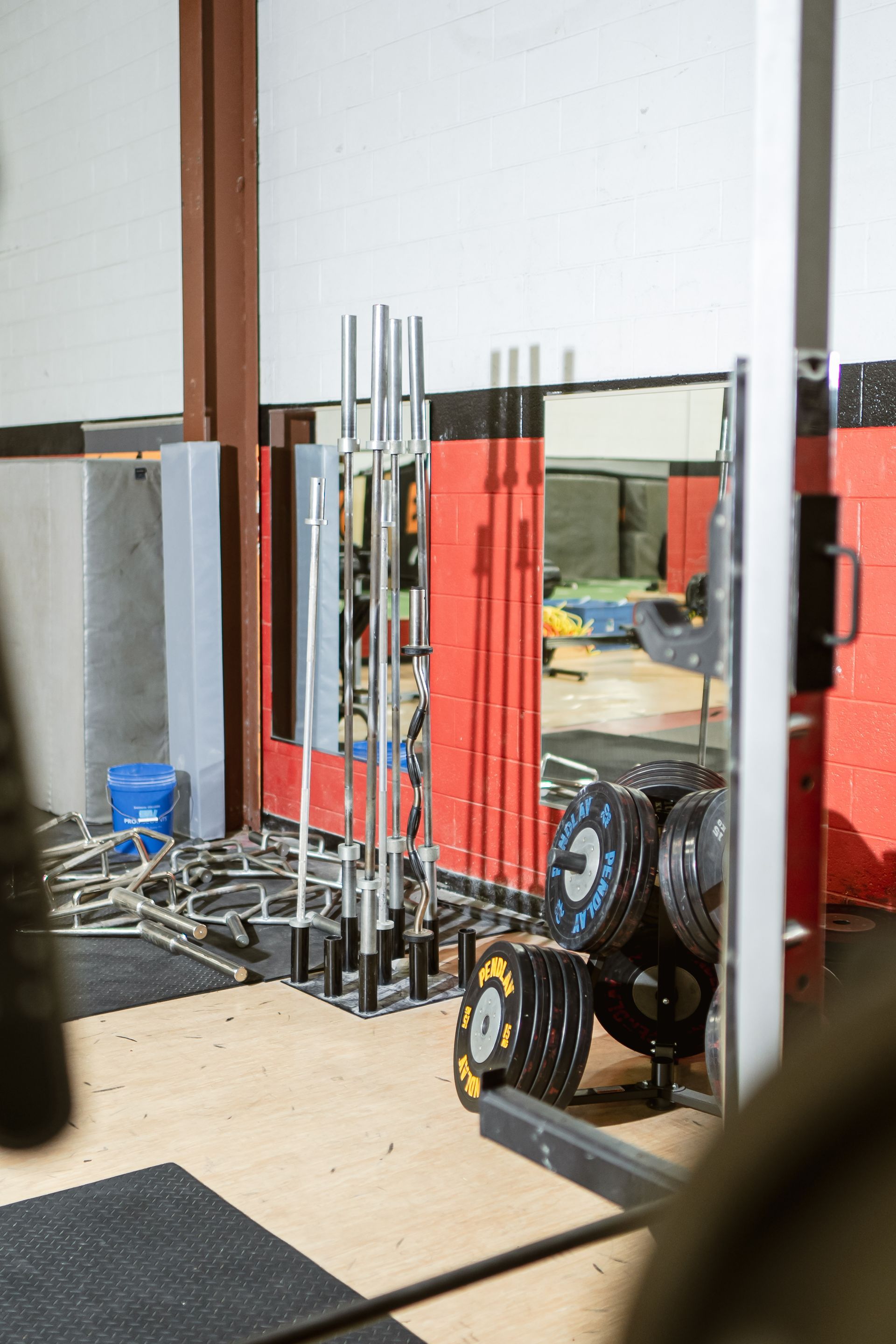 Indoor gym corner with weightlifting bars, plates, and mirrors against a white wall