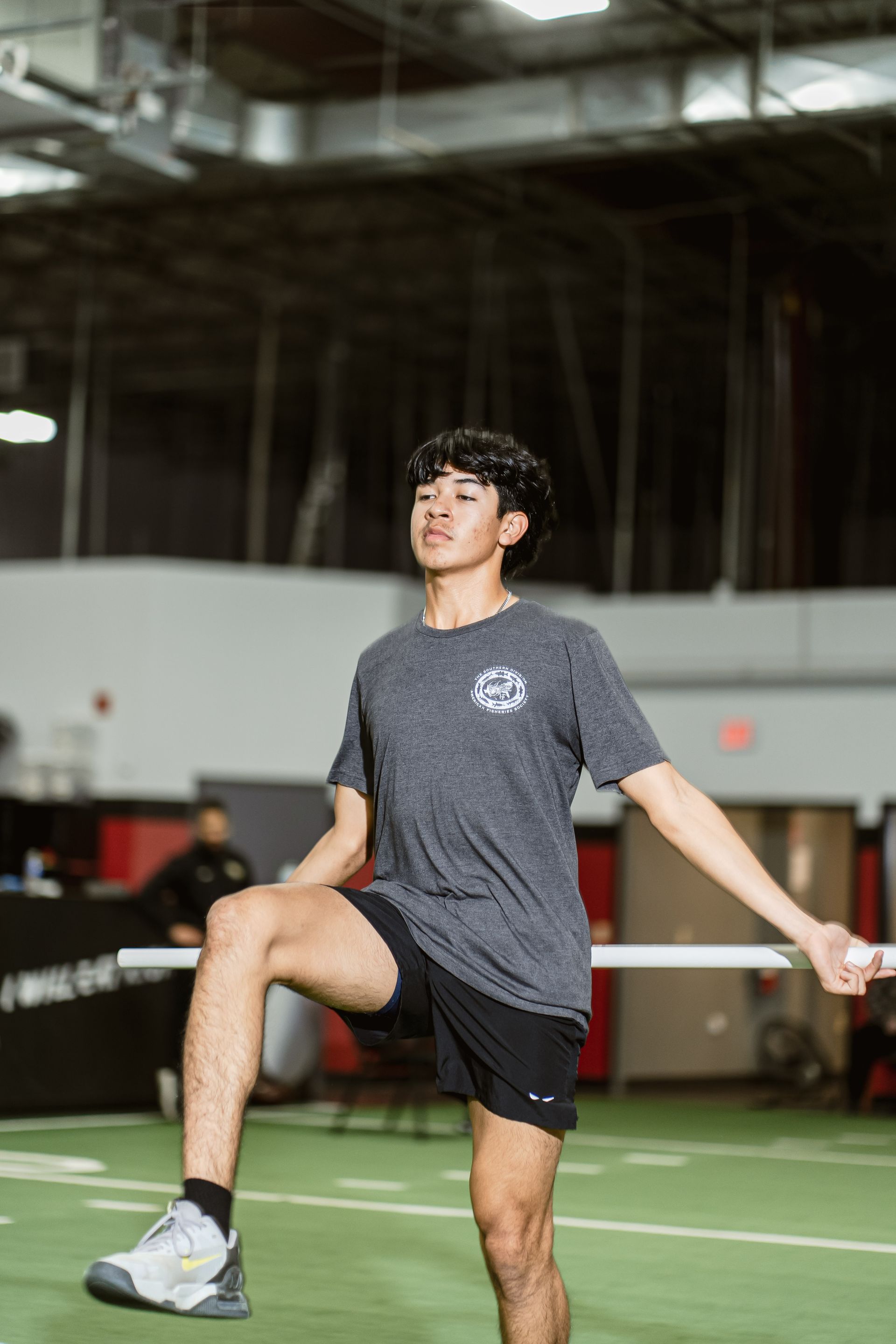 Athlete stretching on indoor turf, lifting one knee and holding a resistance band.