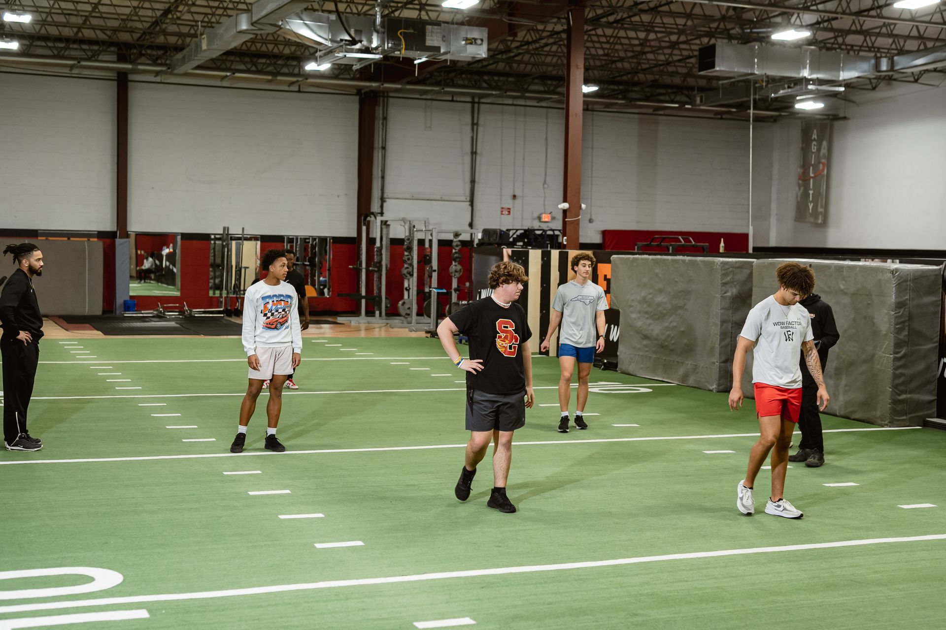 Several people standing on an indoor turf field near a lacrosse goal in a gymnasium