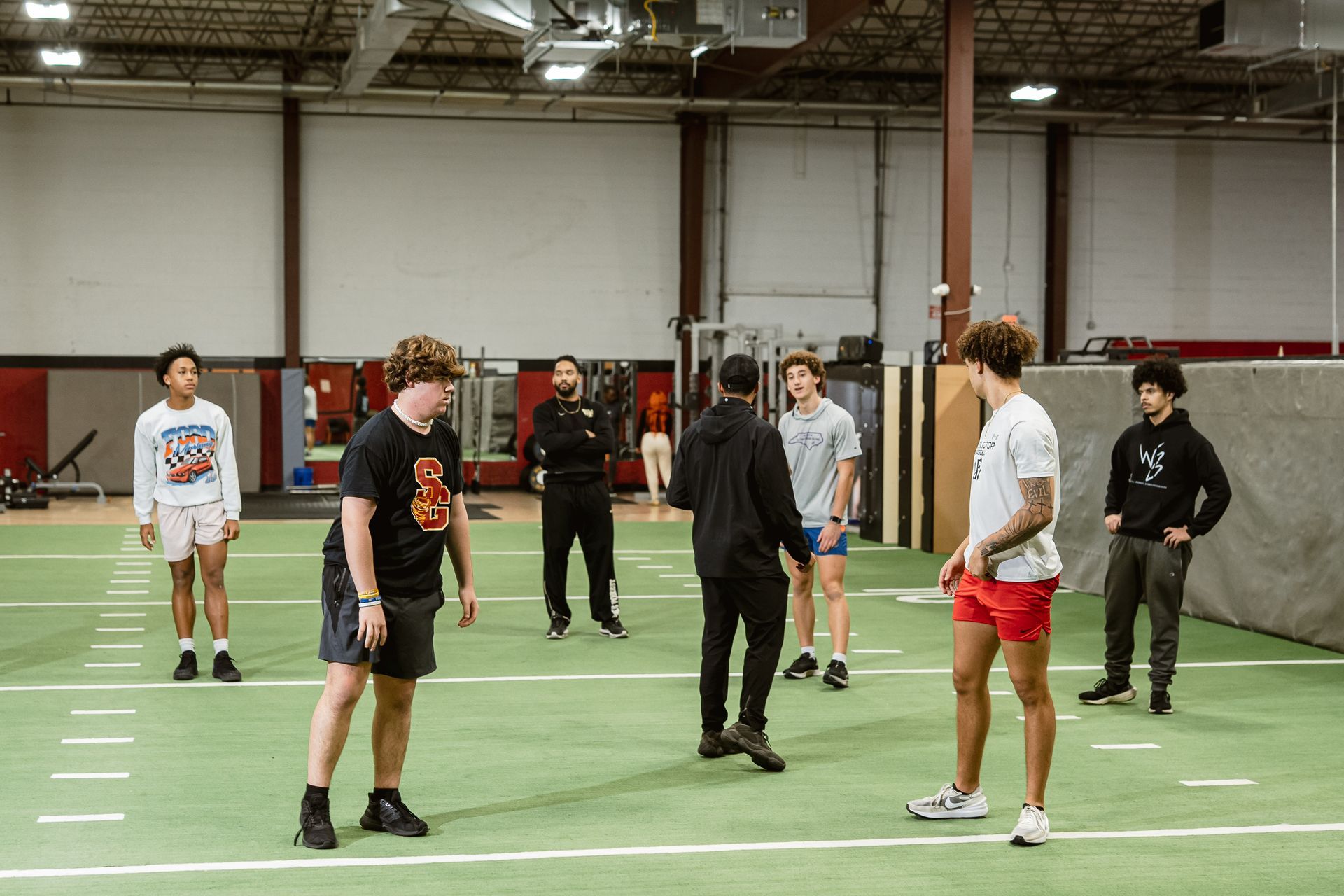 People standing in a gym, spaced apart on a green indoor sports court.