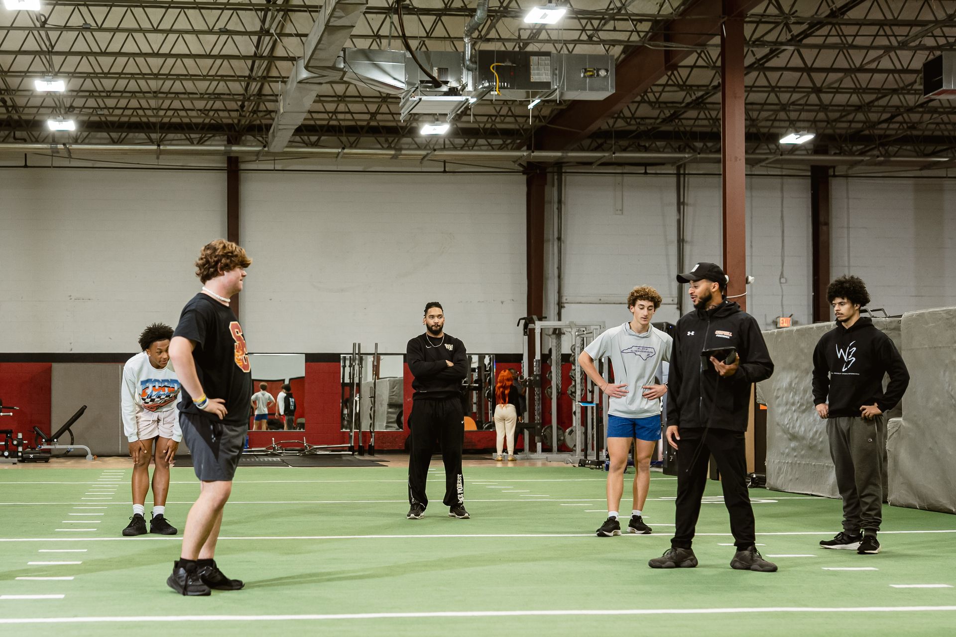 People standing in an indoor gym, facing each other on a turf field.