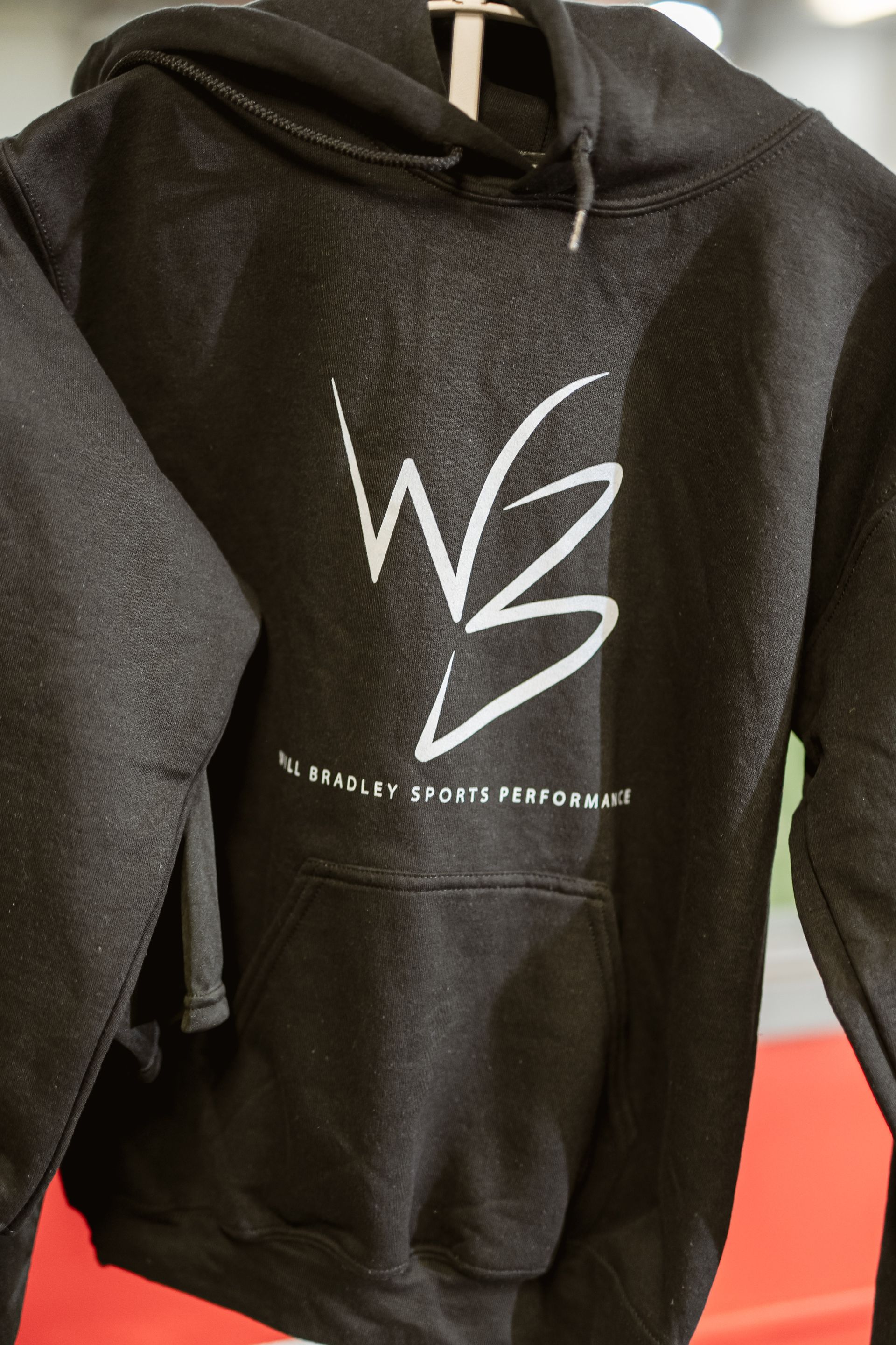 Black hoodie with white logo and small text on the front, hanging on a display rack.