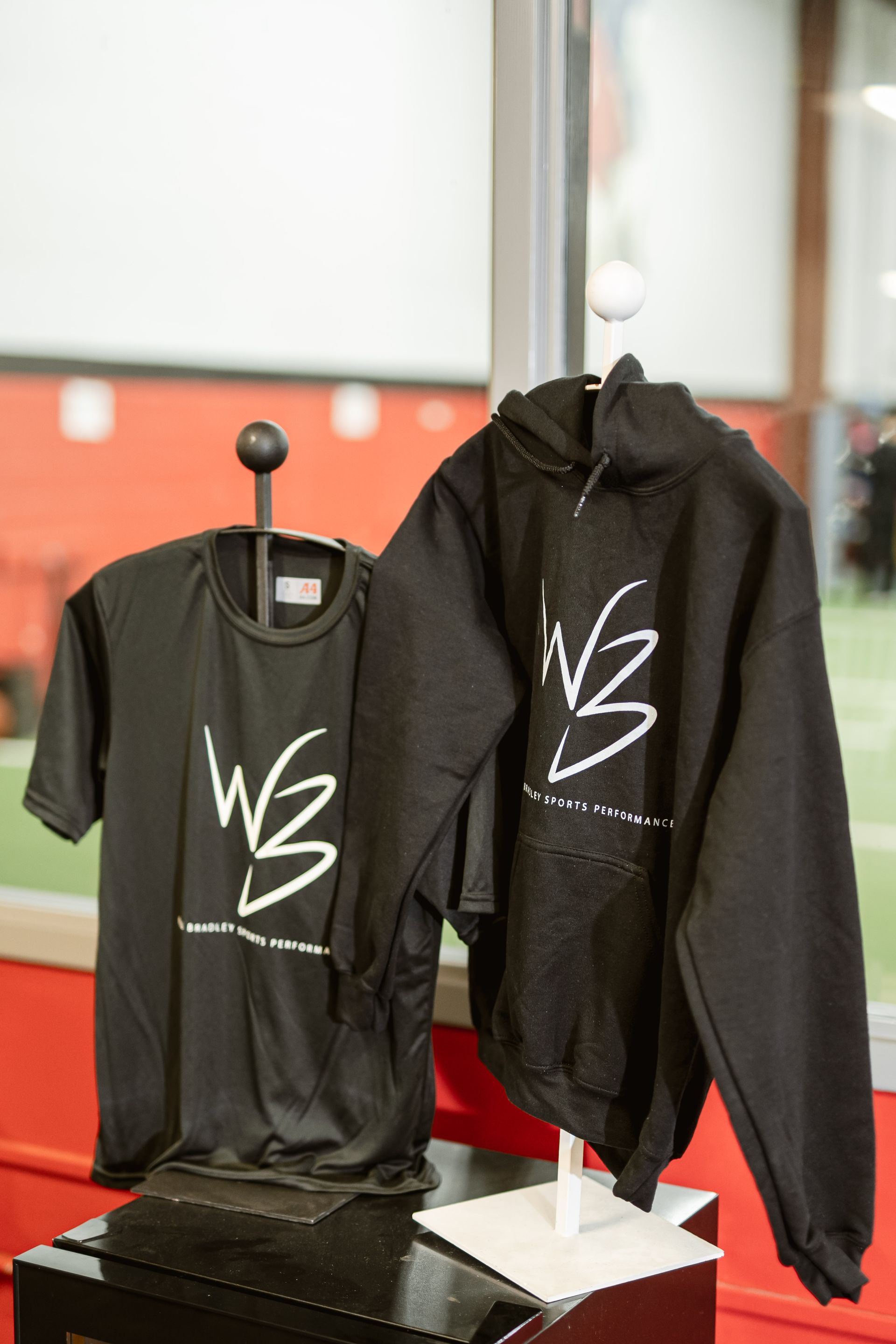 Black T-shirt and black hoodie with white logo displayed on stands in a store.