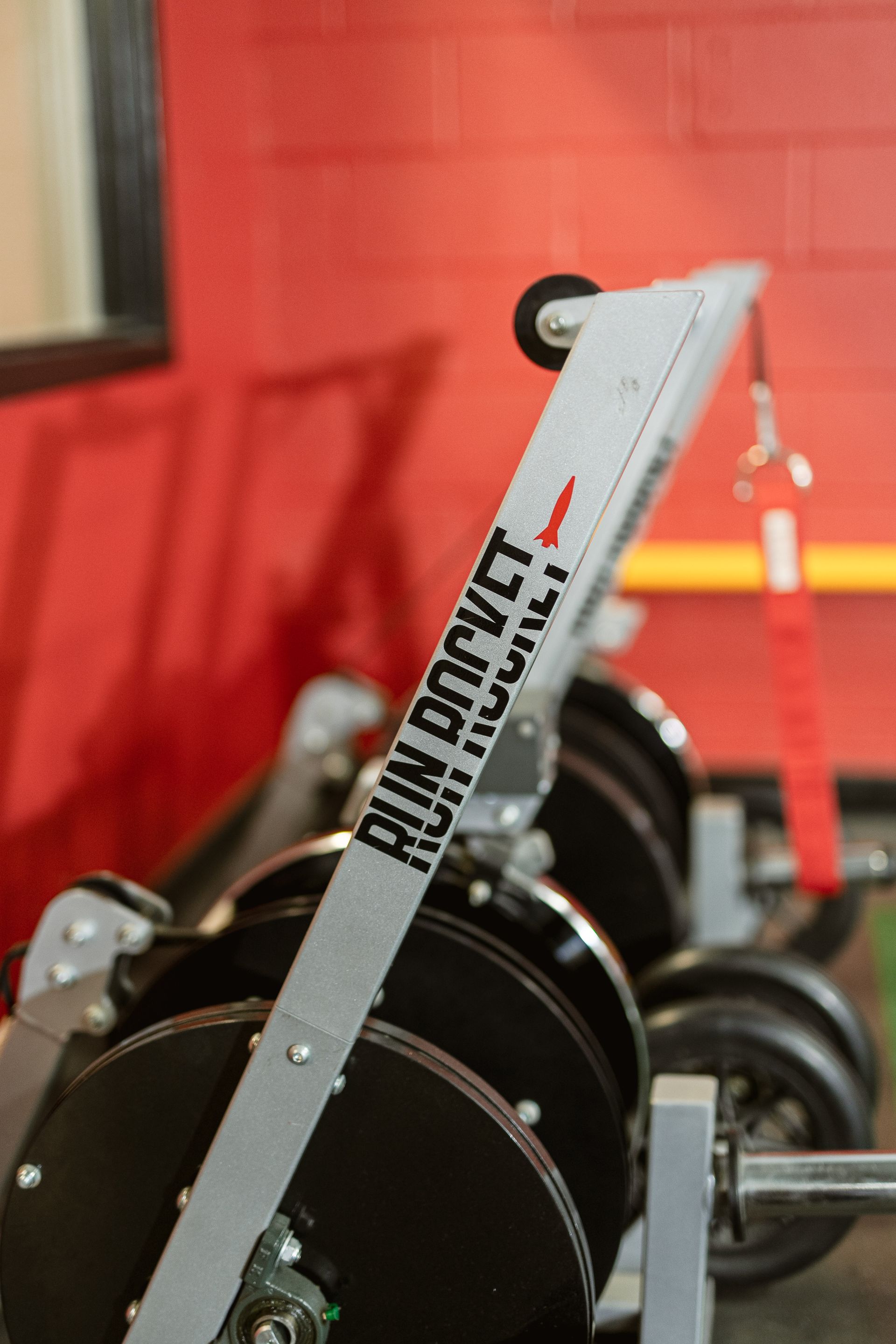 Weightlifting machine with black weights and a white frame against a red wall.