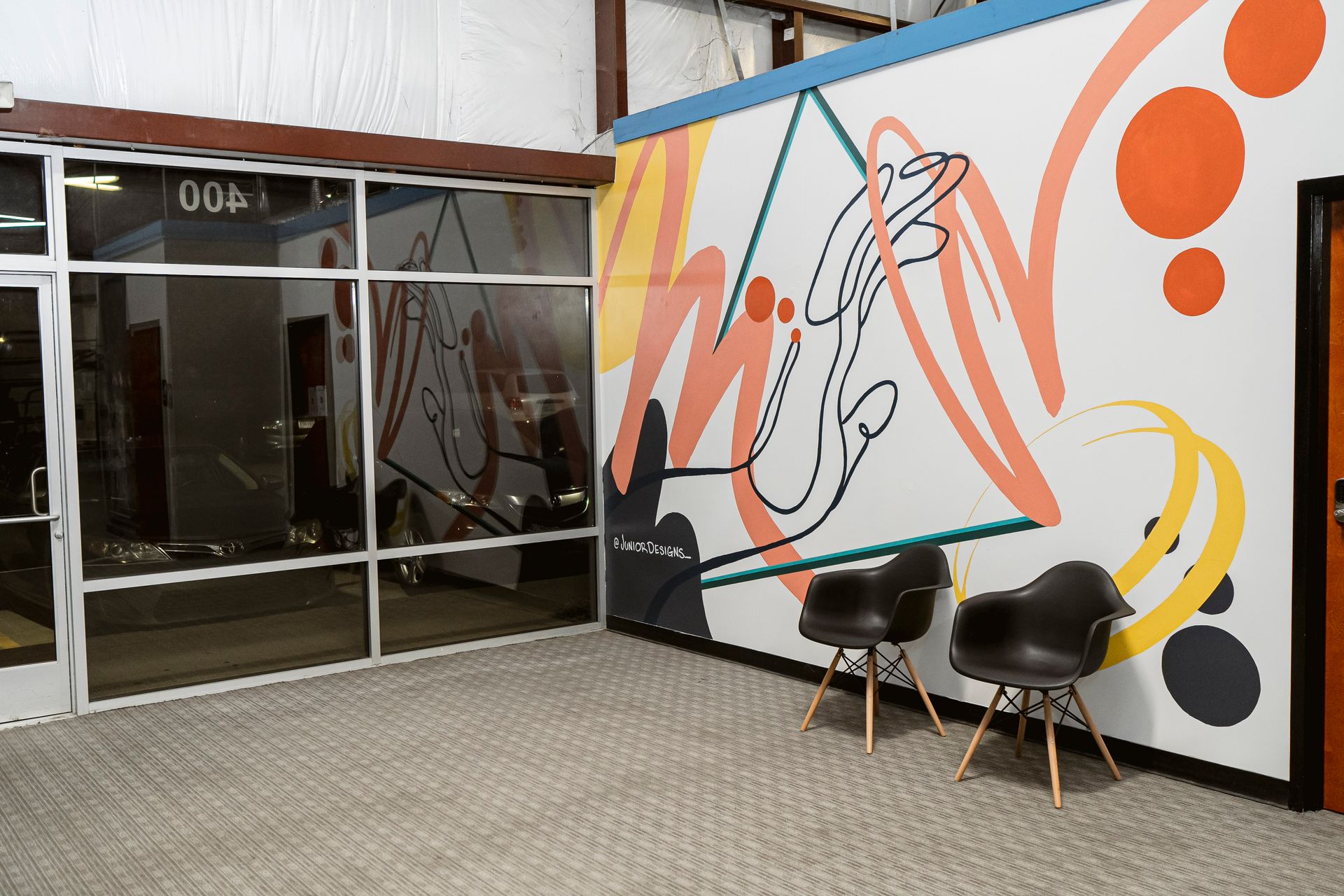 Modern hallway with colorful abstract mural, glass doors, and two black chairs on a tiled floor