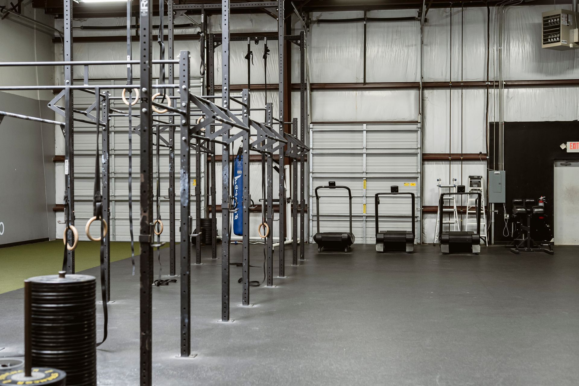 Empty industrial gym with metal rigs, hanging bars, and a gray concrete floor
