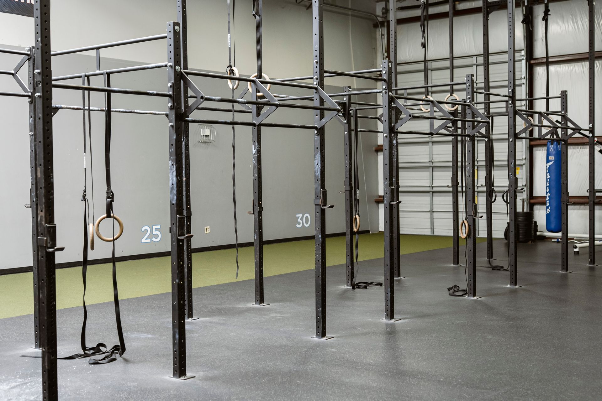 Indoor gym with black pull-up rigs, hanging rings, and numbered stations on a gray floor