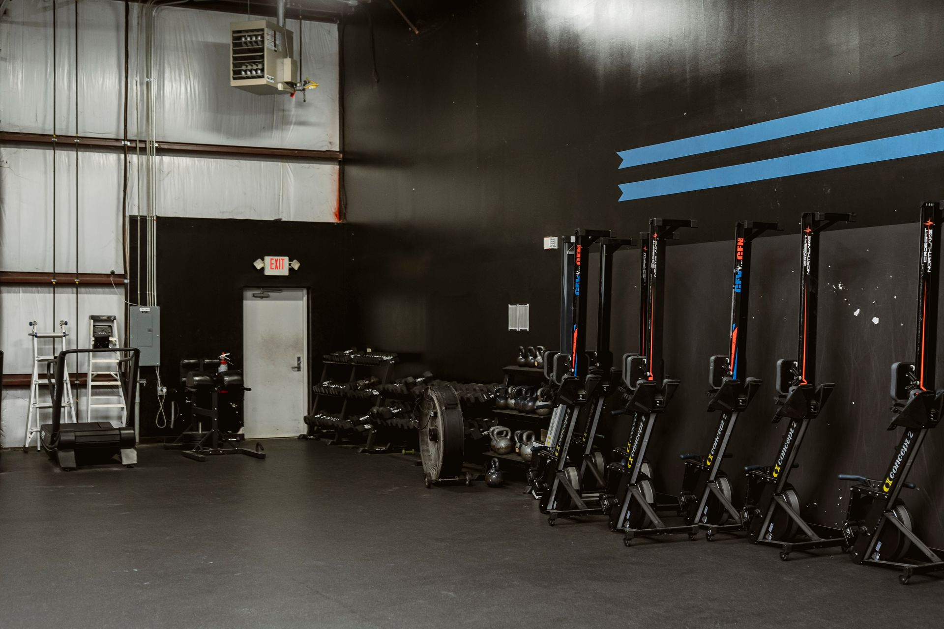 Empty gym with rowing machines lined up against a dark wall and blue stripes.