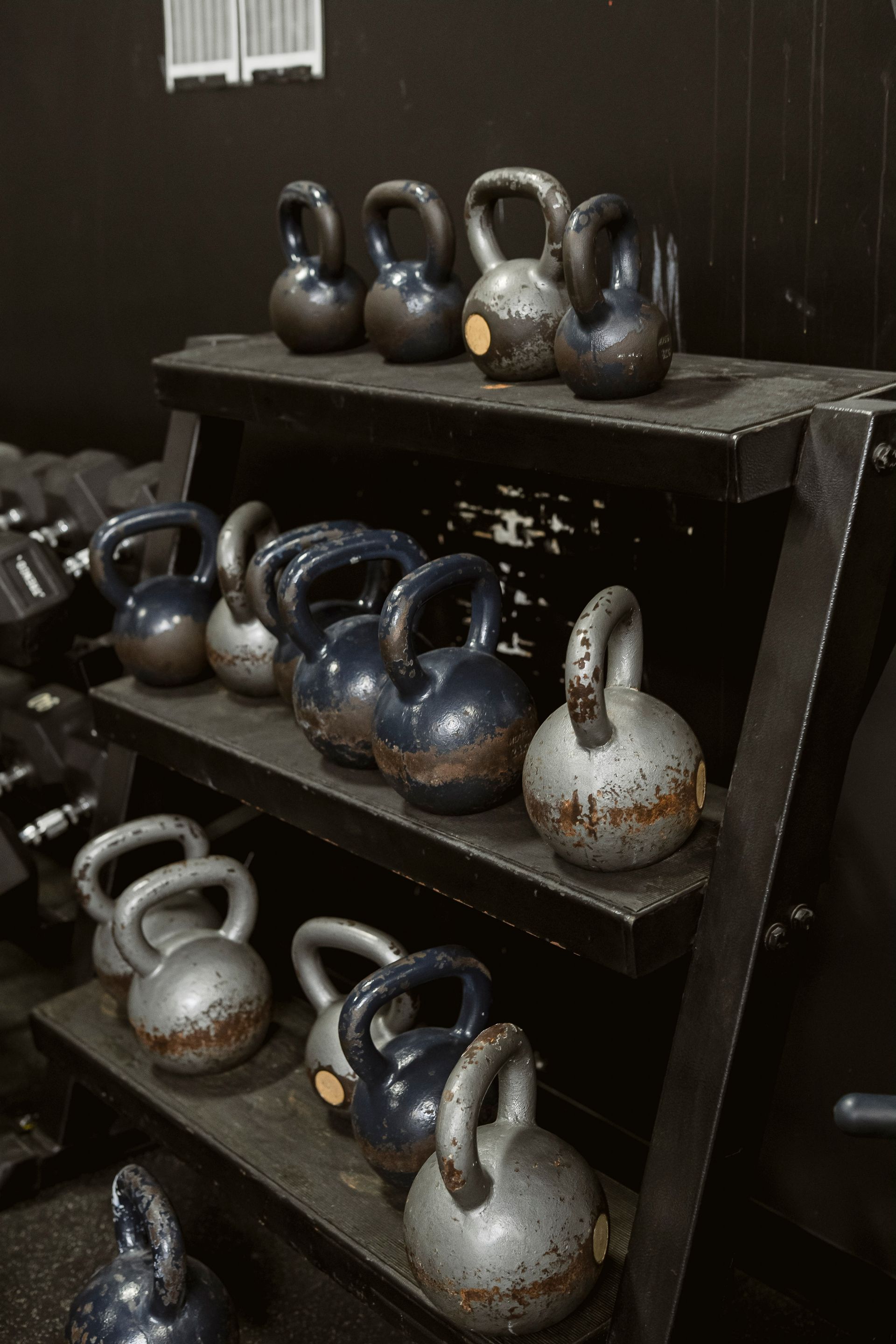 Several kettlebells arranged on a black metal rack in a gym.