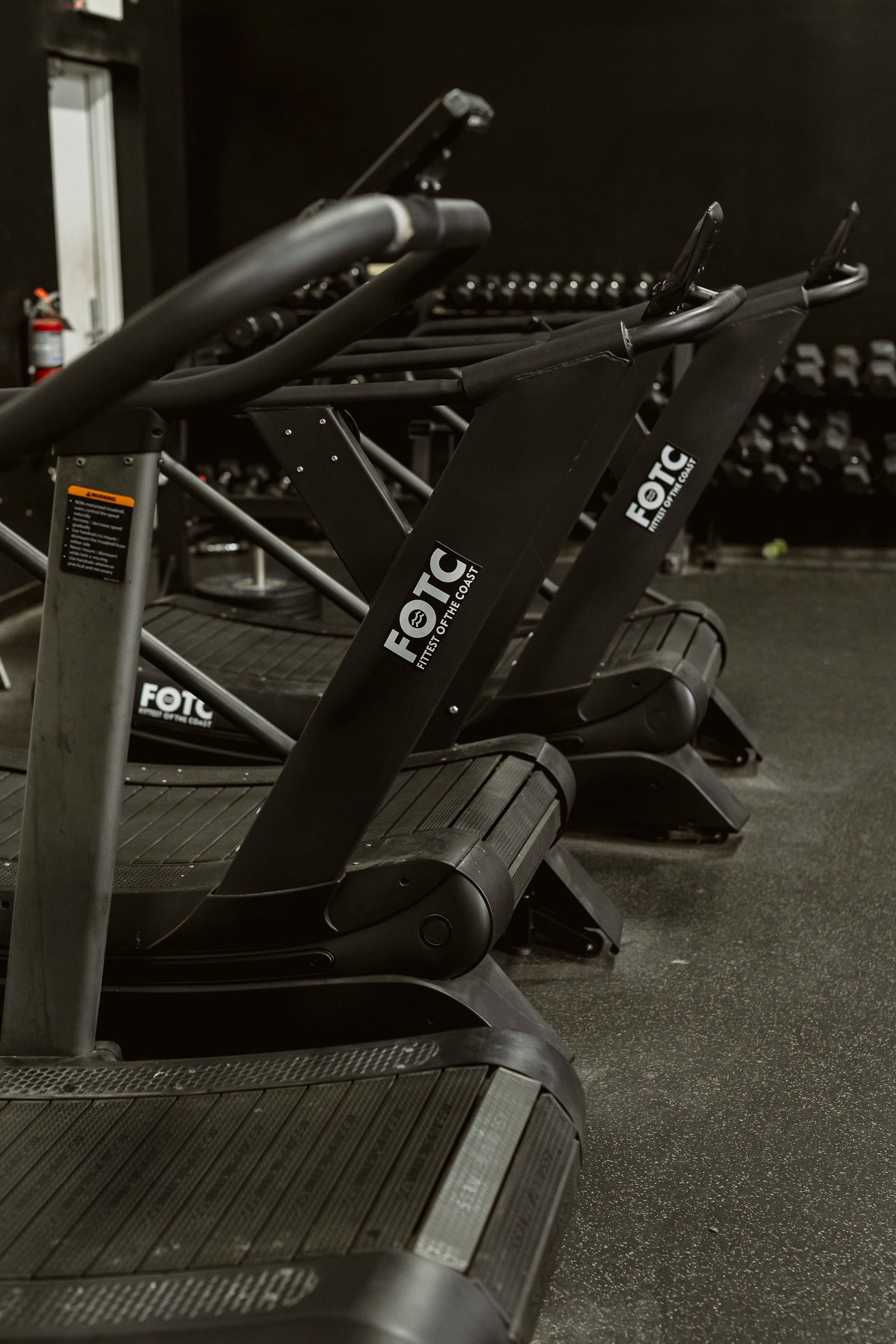Row of black treadmill machines in a dimly lit gym