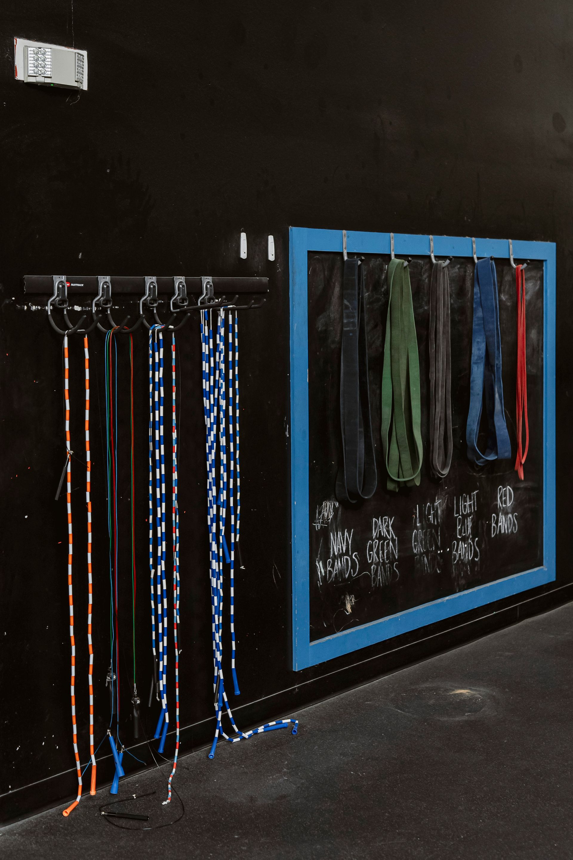 Black wall with hanging colorful lanyards and straps on hooks, framed by a blue border panel.