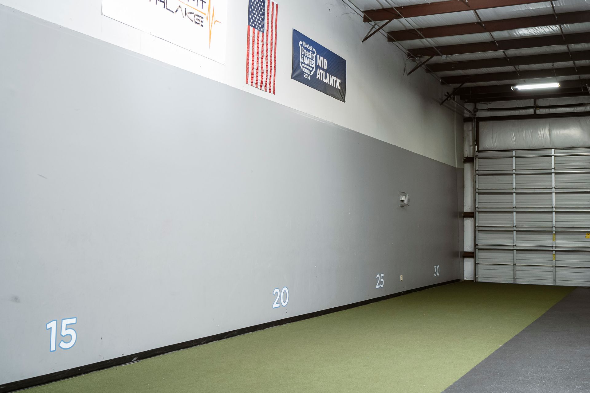 Empty indoor warehouse with gray wall, green turf floor, and large roll-up door