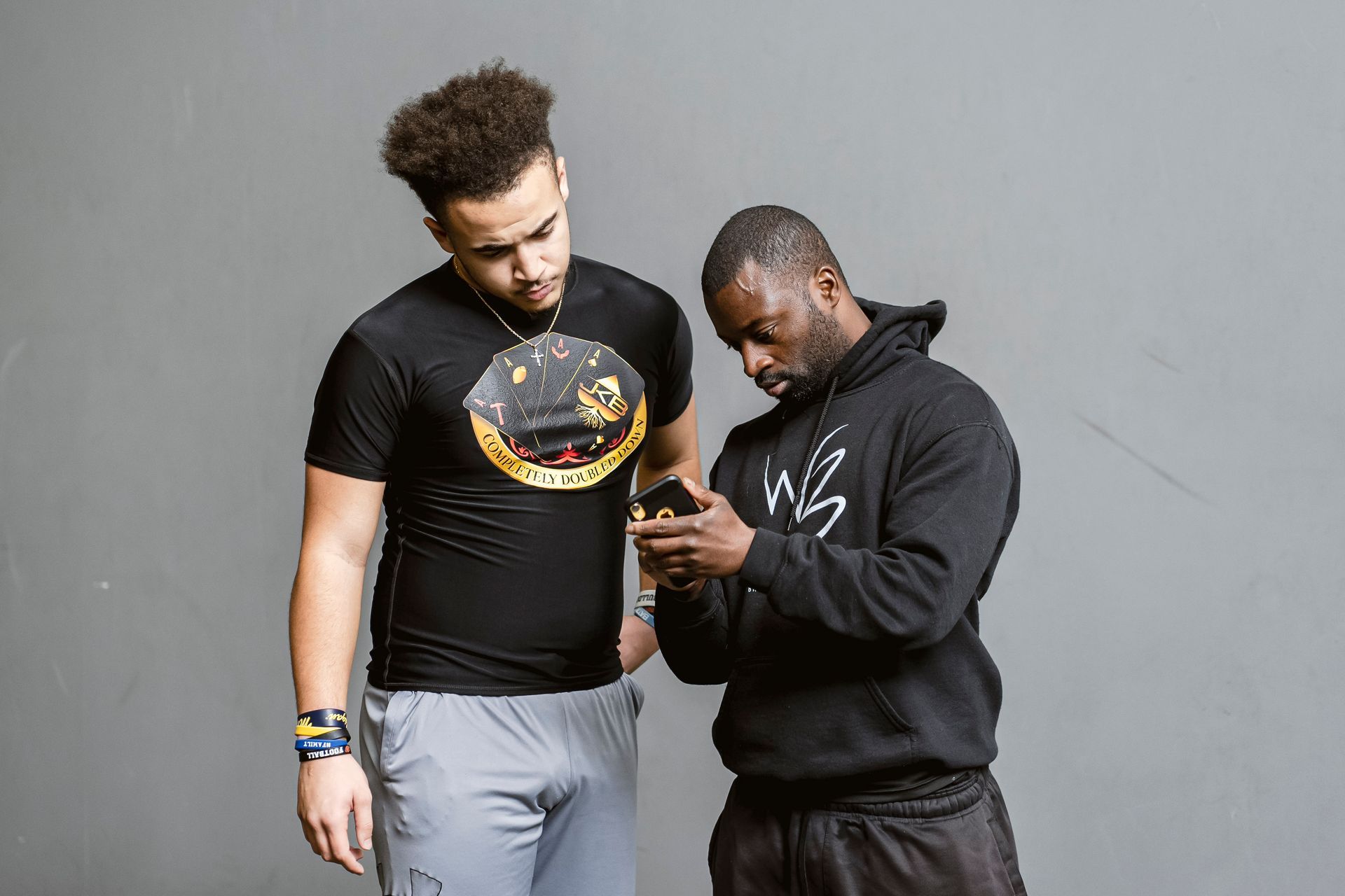 Two men standing and looking at a phone, one pointing at the screen against a gray background