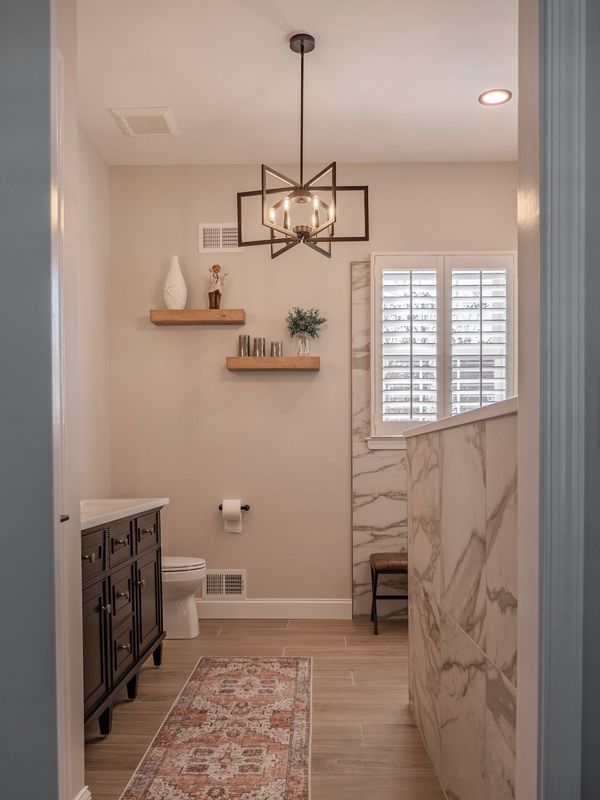 Bathroom with black vanity, patterned rug, wooden shelves, marble accent wall, and geometric light fixture.