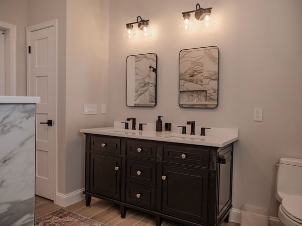Bathroom with dark vanity, marble countertop, two mirrors, and sconces.
