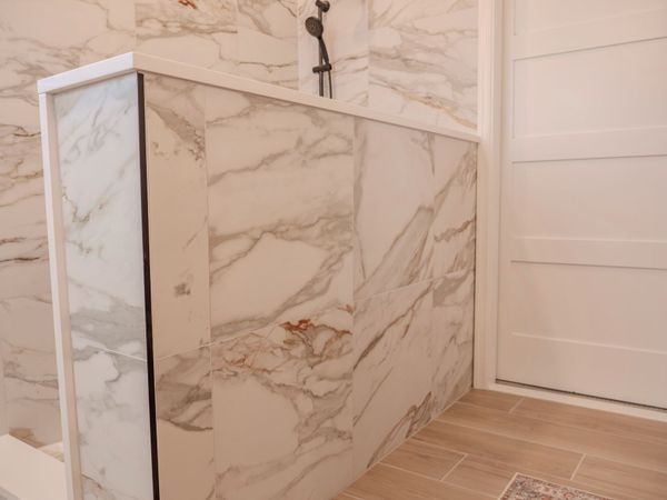 Bathroom with marble-look tile walls, a showerhead, and a white door, with light brown tile flooring.