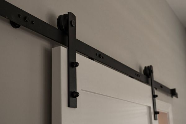 Black metal barn door track installed on a white wall, supporting a white door.
