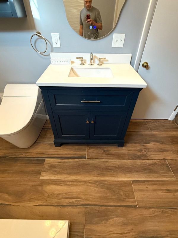 Bathroom with blue vanity, white countertop and sink, wood-look floor, and a mirror.