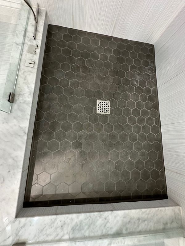 Shower with dark gray honeycomb tile floor, white and gray walls, and a drain.