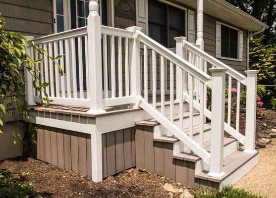 White railing and stairs leading up to a house entrance; brown deck base and steps.