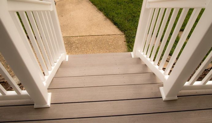 White railing frames gray deck steps leading to a concrete path and lawn.