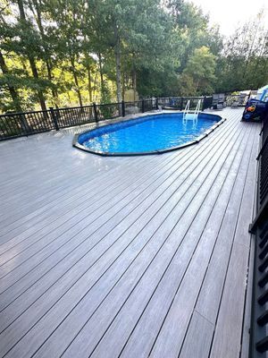 Gray composite deck surrounds oval pool. Black railing, trees in background.