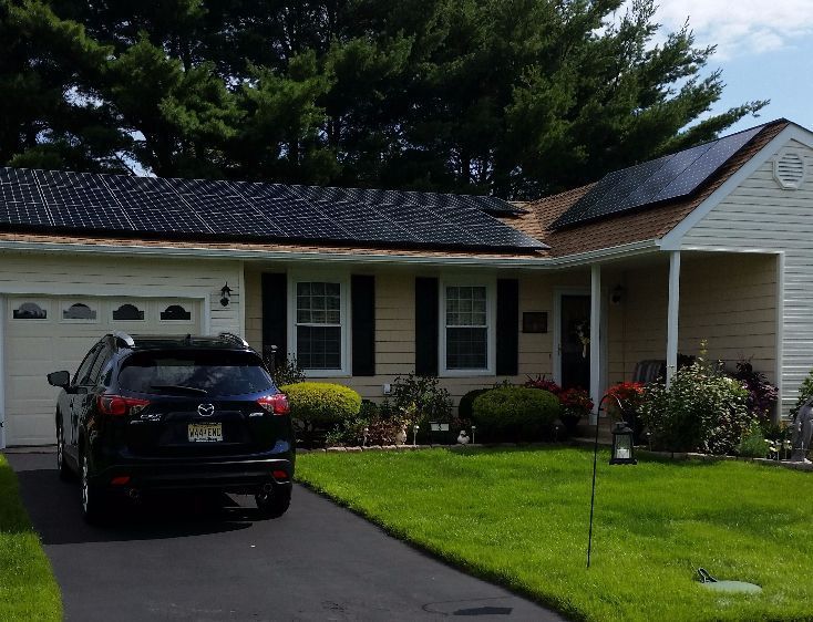 Black solar panels on a house roof with a car parked in front.
